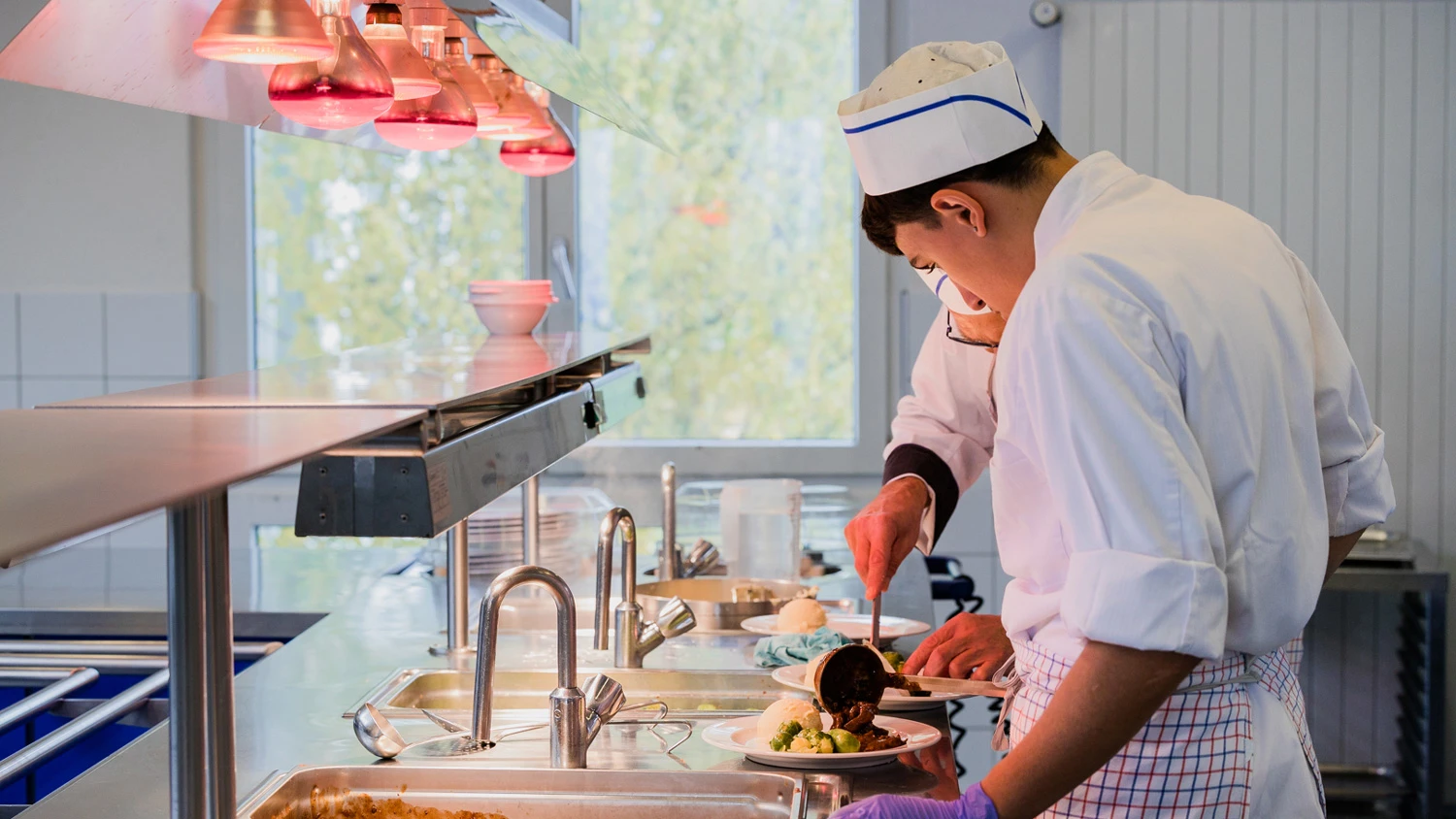 Junger Auszubildender bei der Zubereitung eines Tellers in einer Großküche.